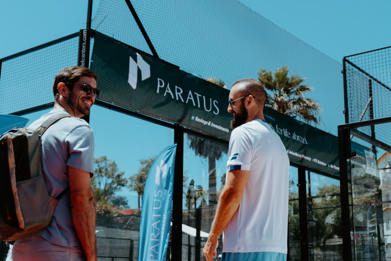 Two padel players in conversation in front of the Paratus Wealth branded backdrop and flag at the tournament